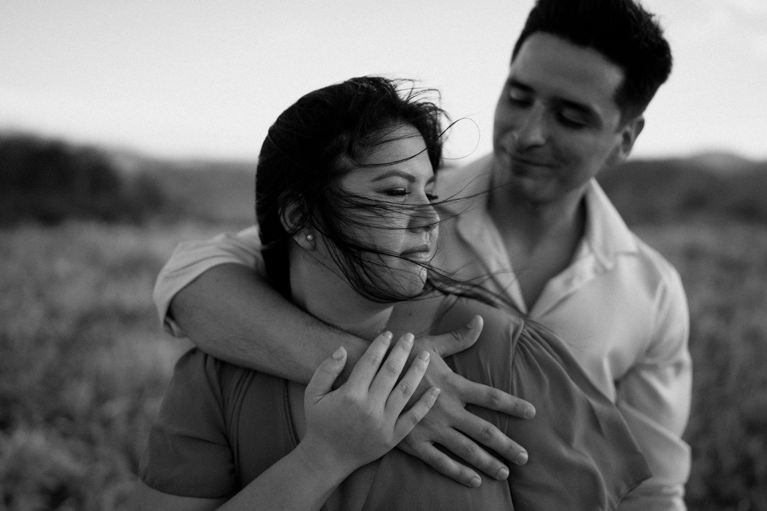 Black and white intimate portrait of a couple embracing in natural outdoor setting.