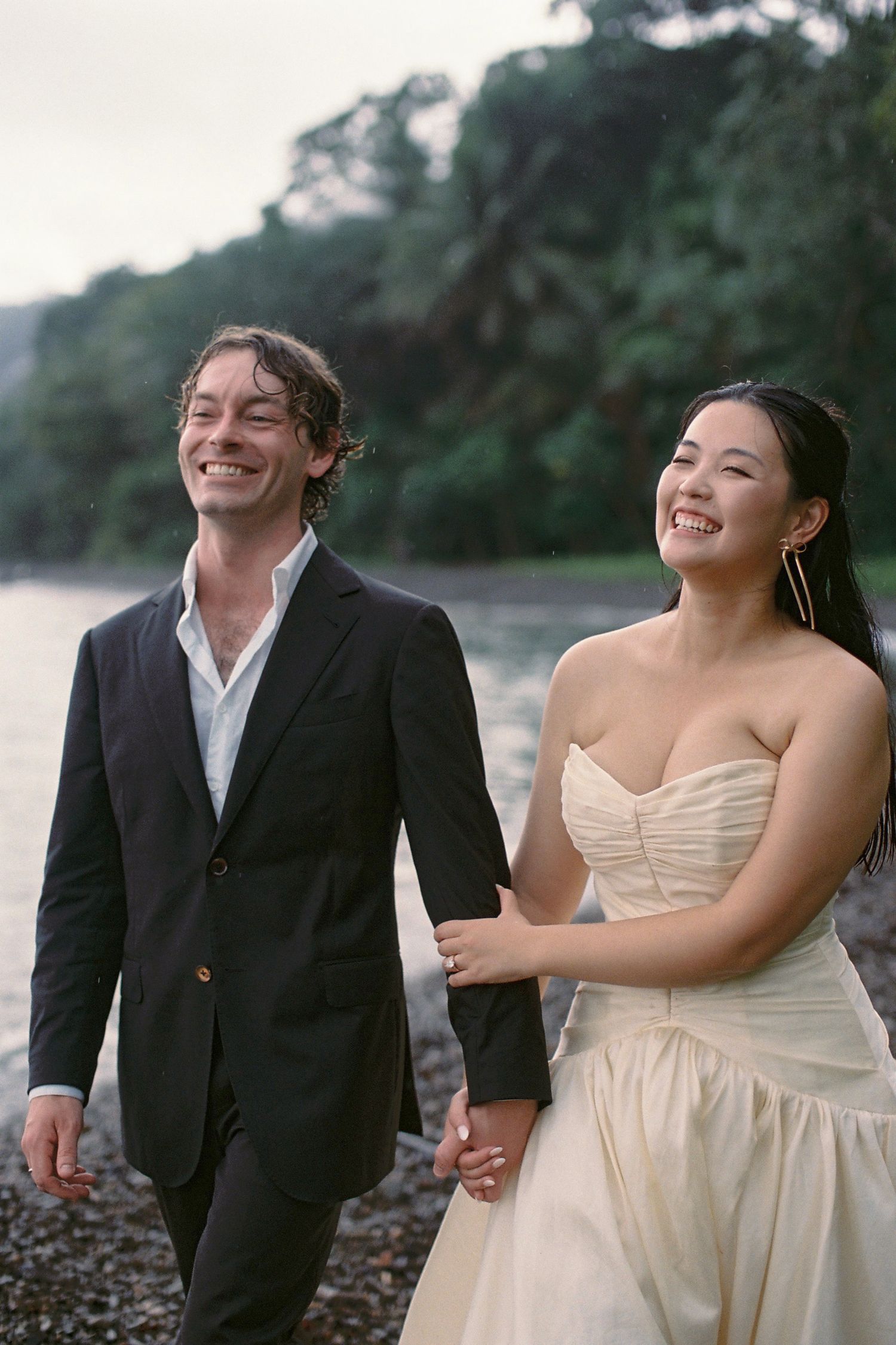 A joyful wedding couple shares a laugh while walking along a tropical beach.