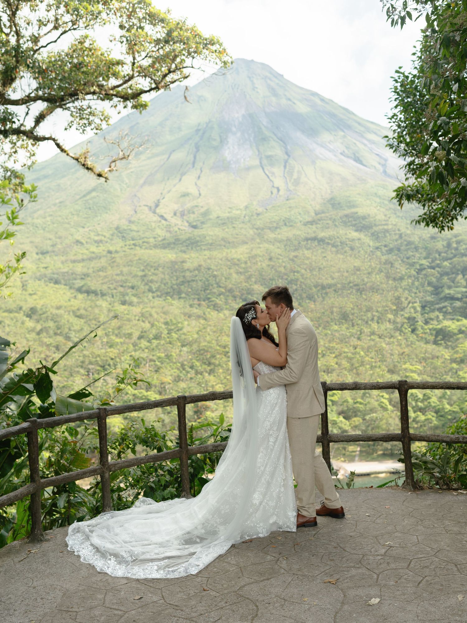 Newlyweds share their first kiss on a mountain viewpoint overlooking a scenic landscape.
