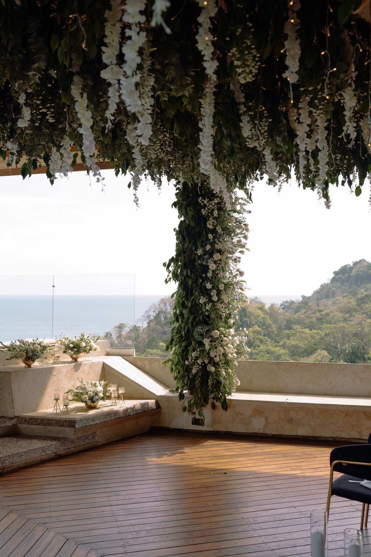 Outdoor wedding venue deck with wooden flooring and floral ceiling decorations overlooking mountains.