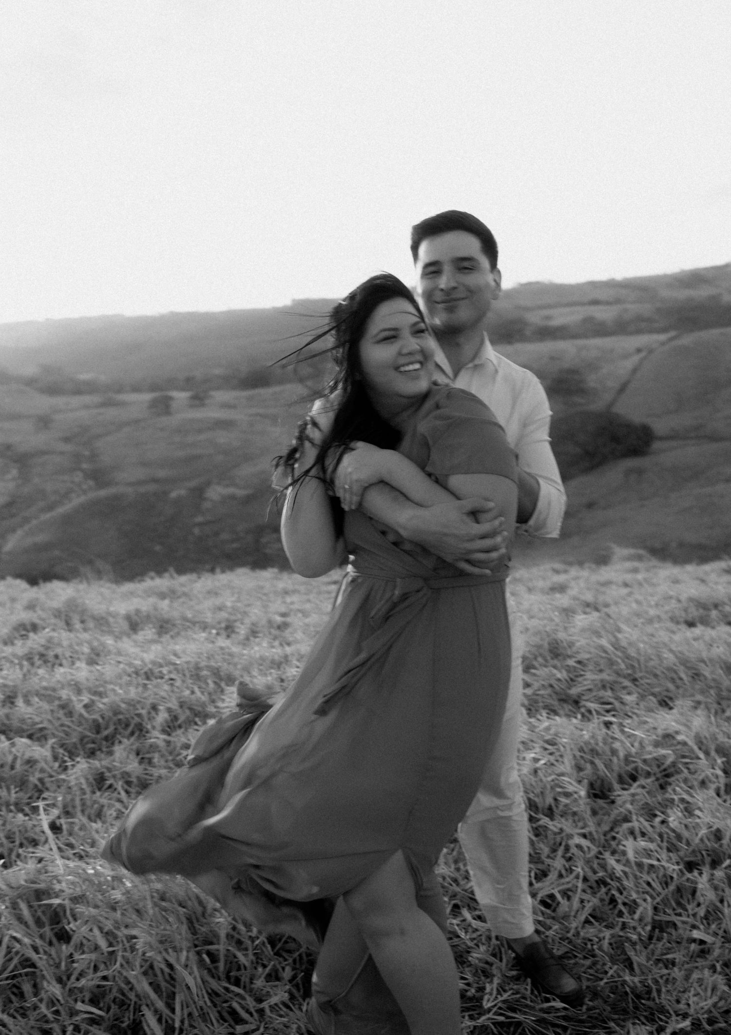 A joyful couple shares a playful moment together in a grassy field.