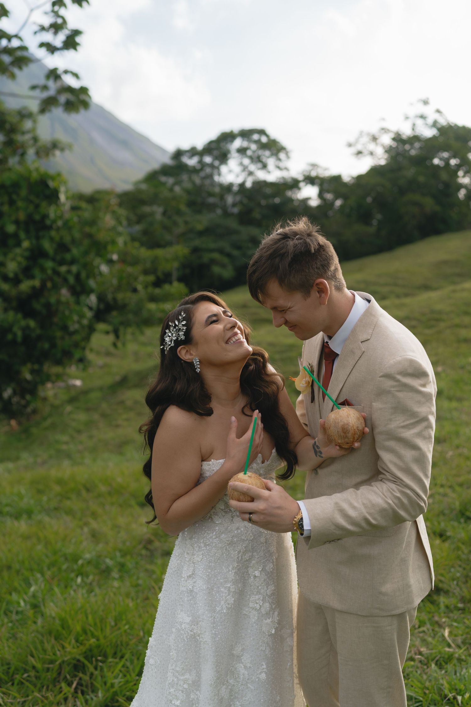 A romantic wedding photo shoot in a lush green field with a mountain backdrop.