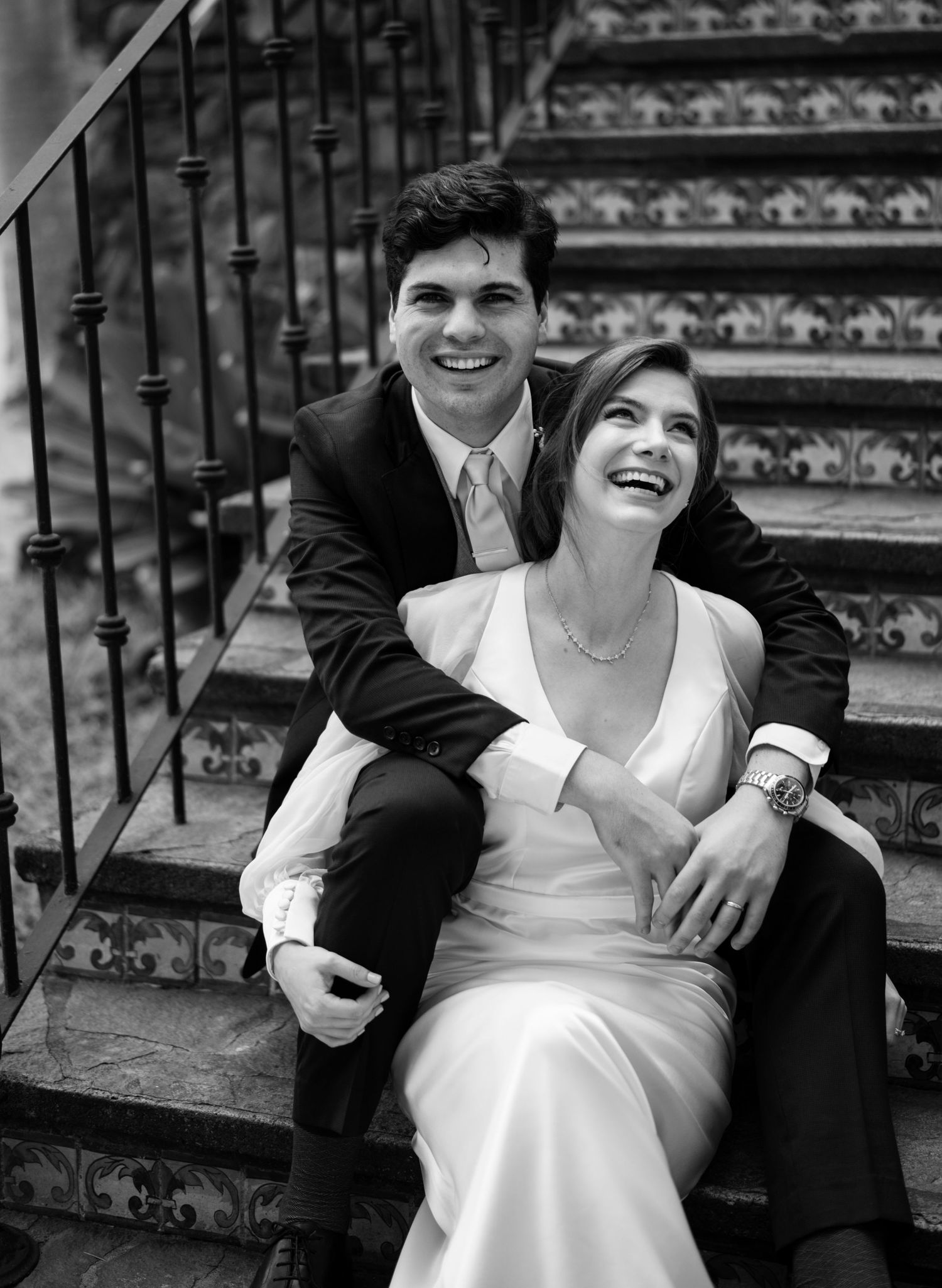 Black and white photo series showing a couple sitting on stone steps sharing joyful laughter and intimate moments together.