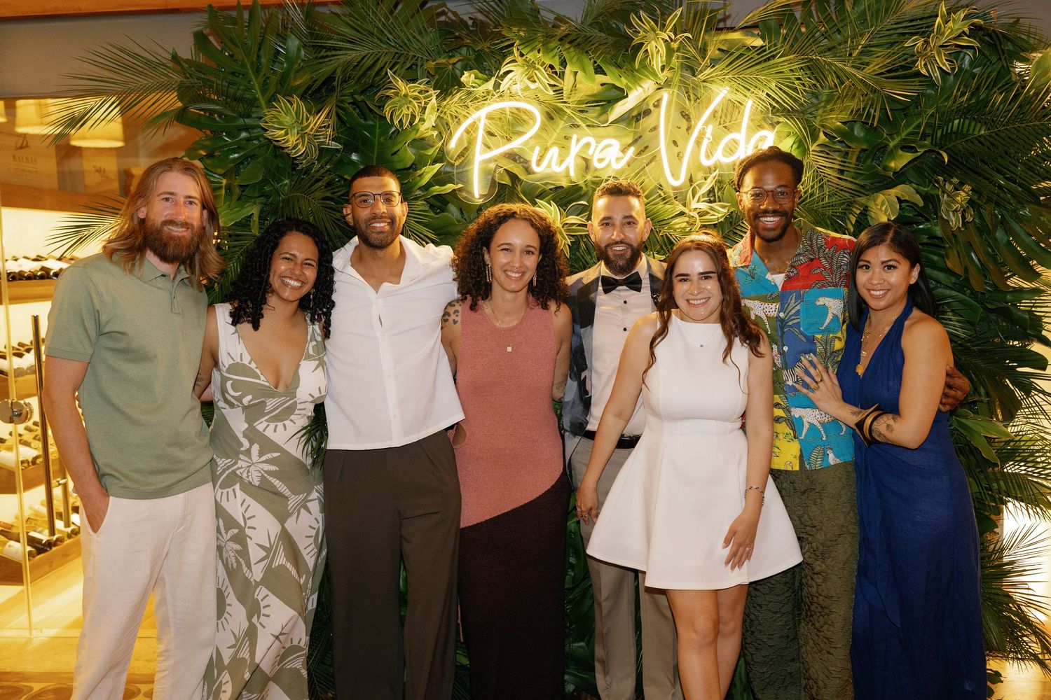 Wedding guests gather under tropical decor and neon signage at an indoor reception venue.