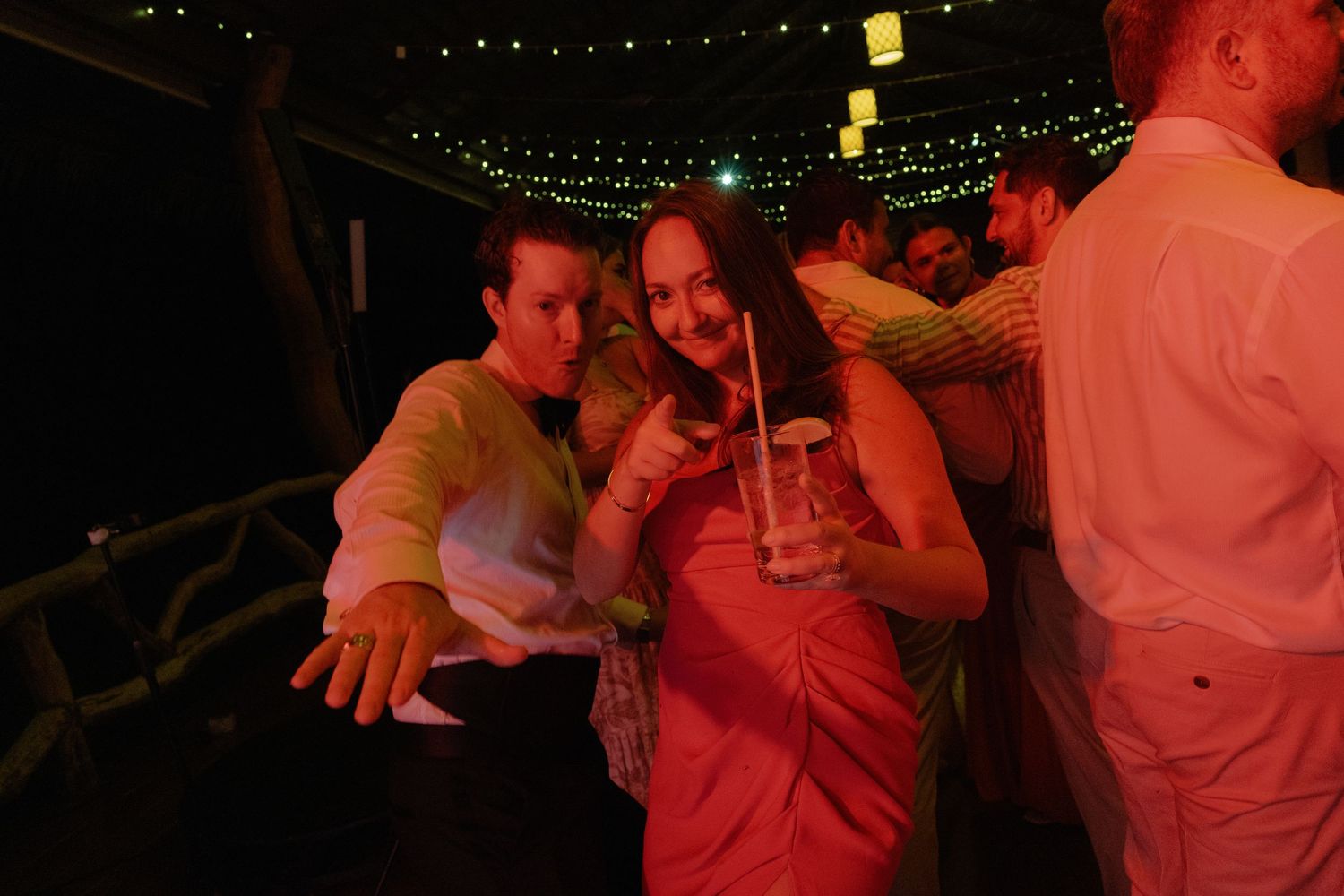 Wedding guests enjoying drinks and dancing under string lights at an evening reception.