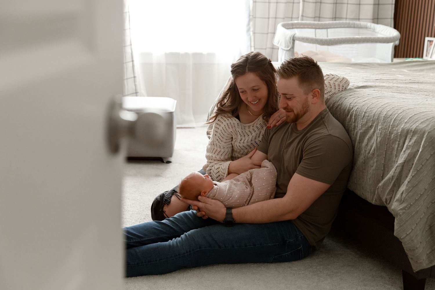 A tender family moment as parents sit on the floor beside their bed bonding with their newborn baby.