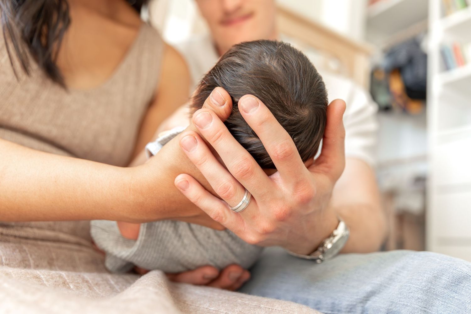 Mother cradling newborn baby's head in her hands, wearing a silver ring, in a soft home setting.