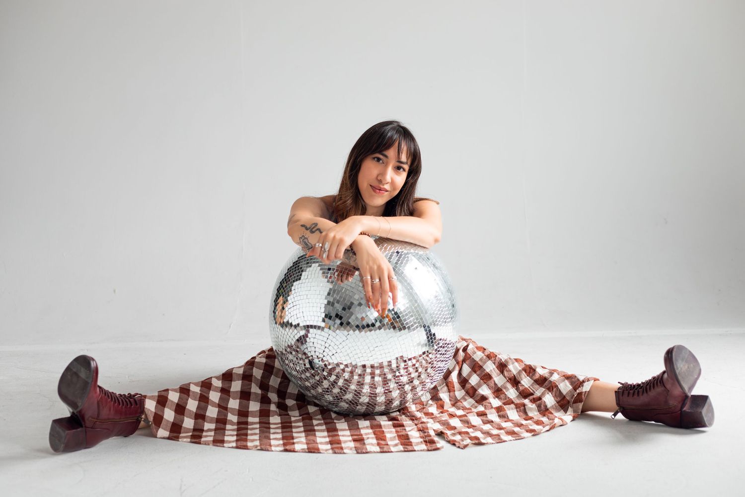 A person in a plaid dress lies on a white studio floor in artistic poses.