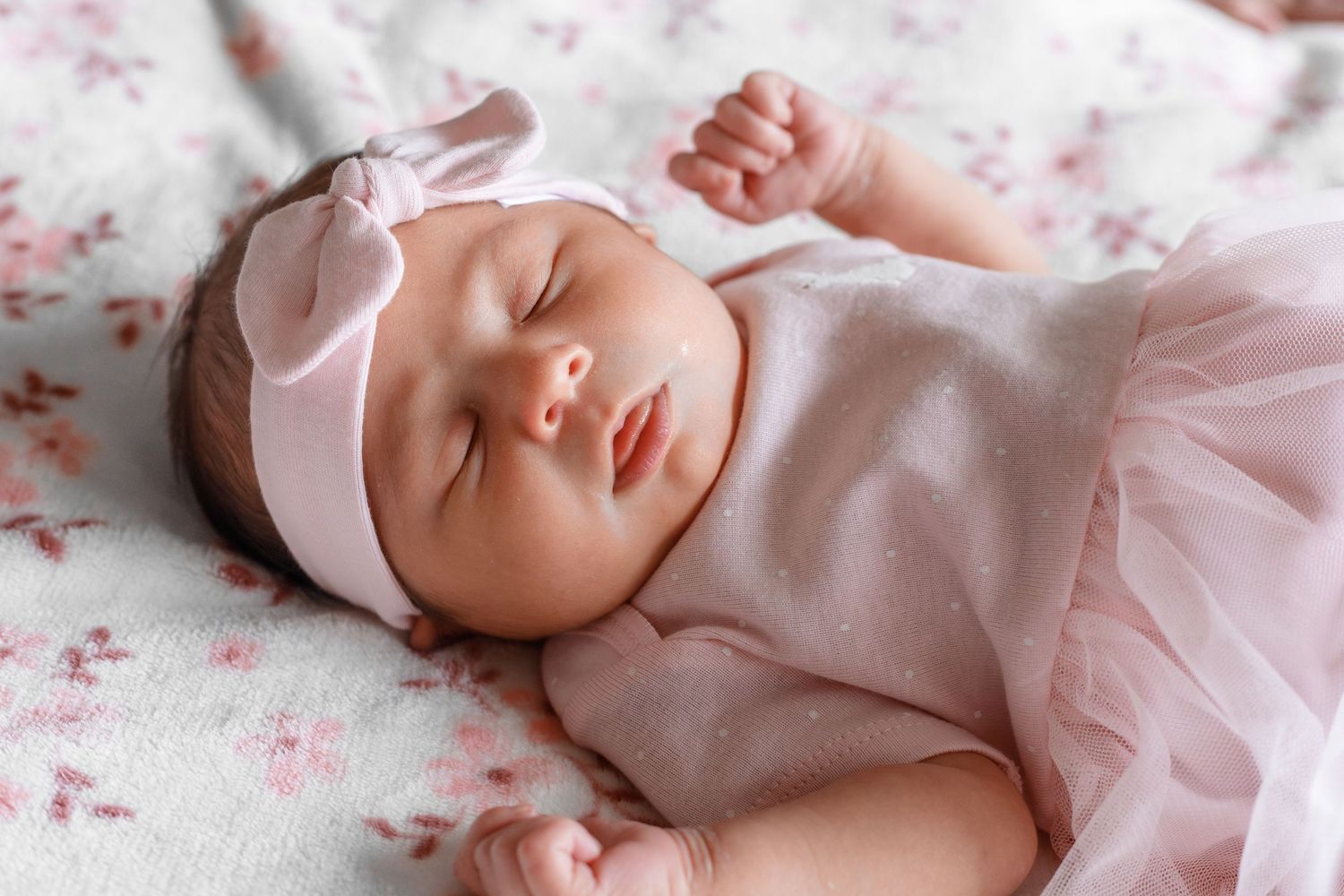 Sleeping newborn baby in pink outfit on floral pattern background.