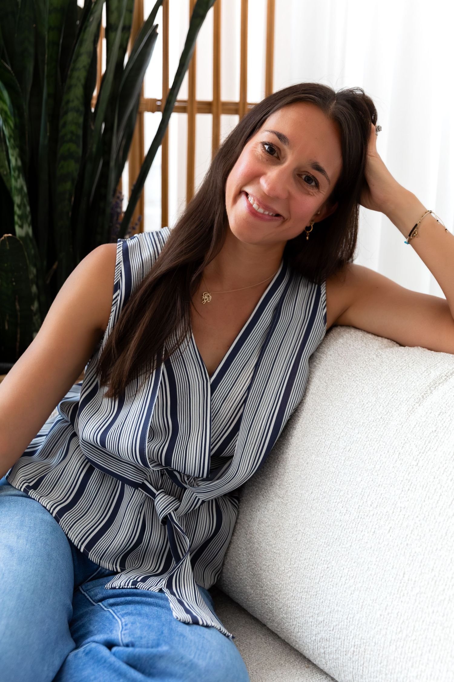 Person in striped wrap top relaxing on white couch with indoor plants.