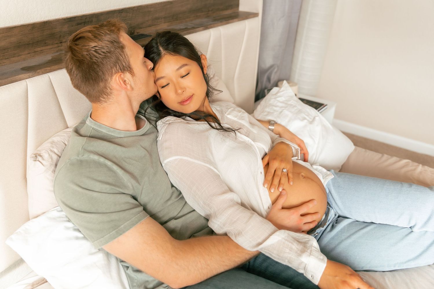 A couple rests together on a couch, with one wearing a sage green shirt and the other in a white button-down shirt.
