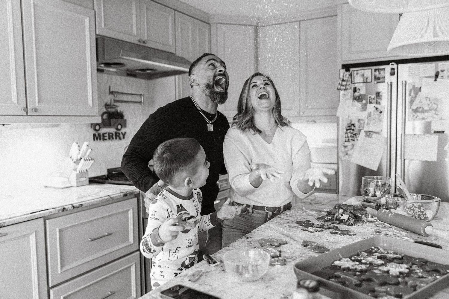 Black and white photo of a joyful family baking holiday cookies together in a cozy kitchen.