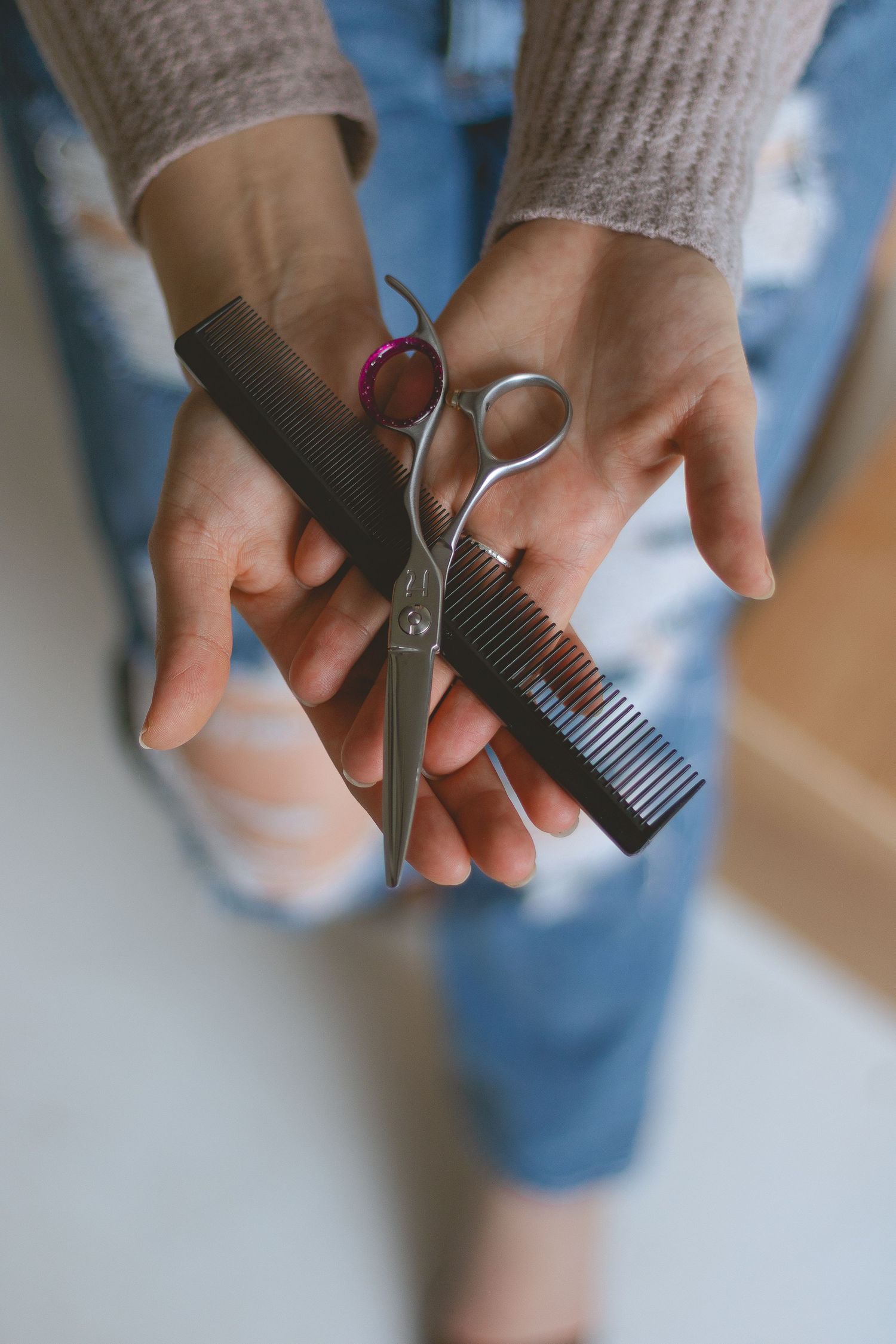Close-up of hands holding professional hairdressing scissors and black comb against denim.