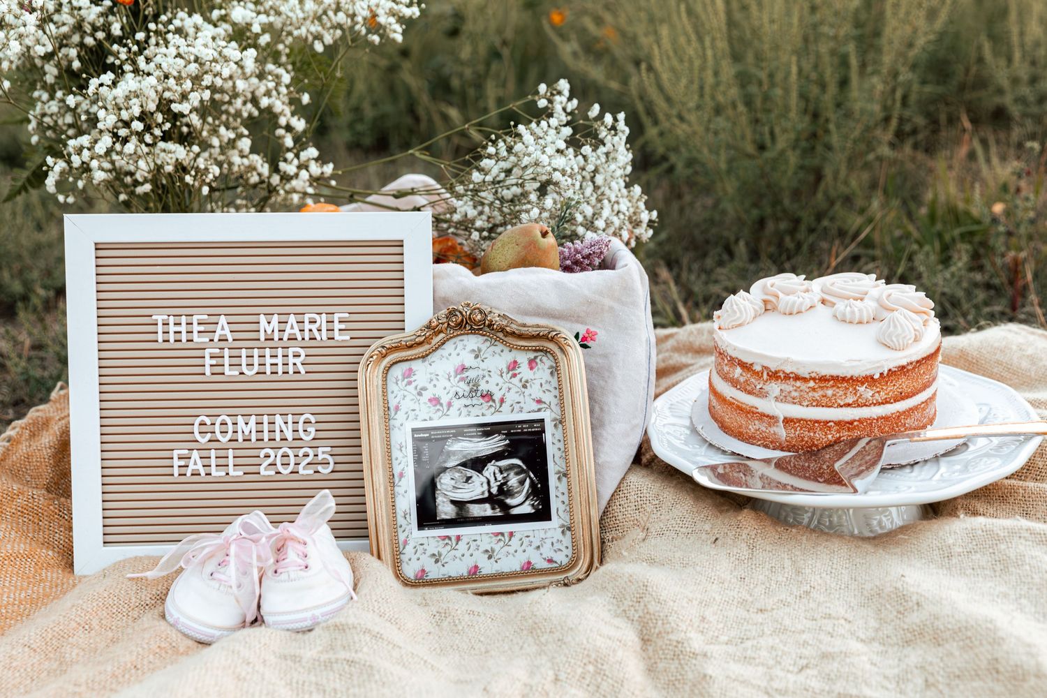 A pregnancy announcement display with letterboard and baby items arranged on a textured backdrop.