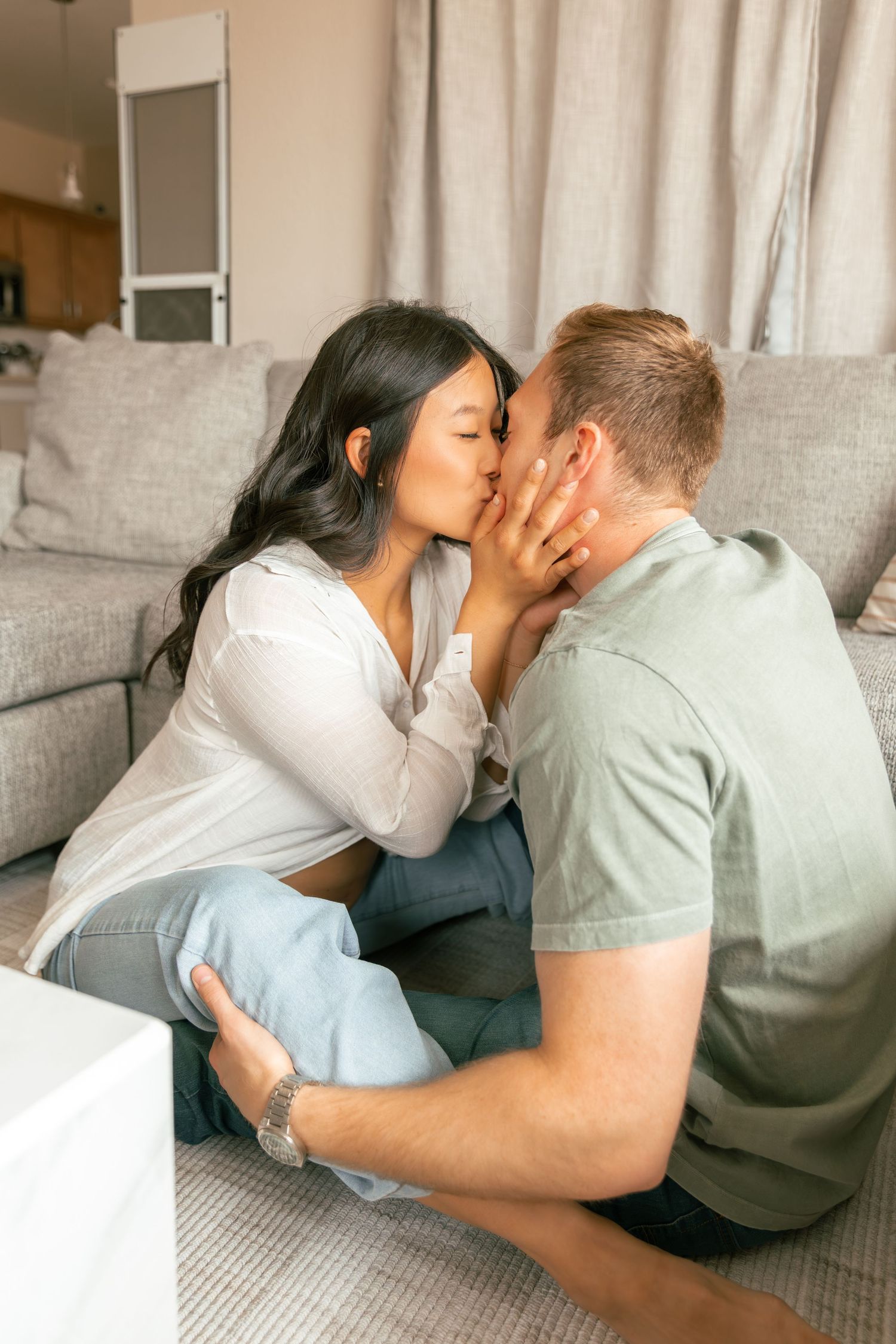 A couple sharing a tender kiss while sitting on the floor in a cozy living room setting.
