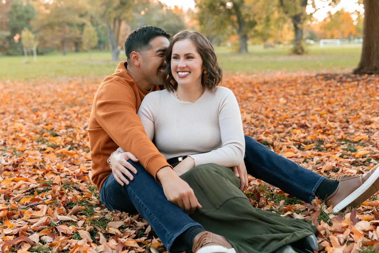 Romantic autumn photoshoot with couple laying in orange fallen leaves.