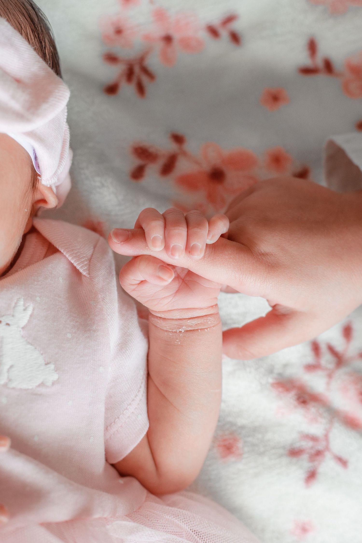 Close-up of tiny baby feet and toes against soft pink fabric with delicate floral patterns.