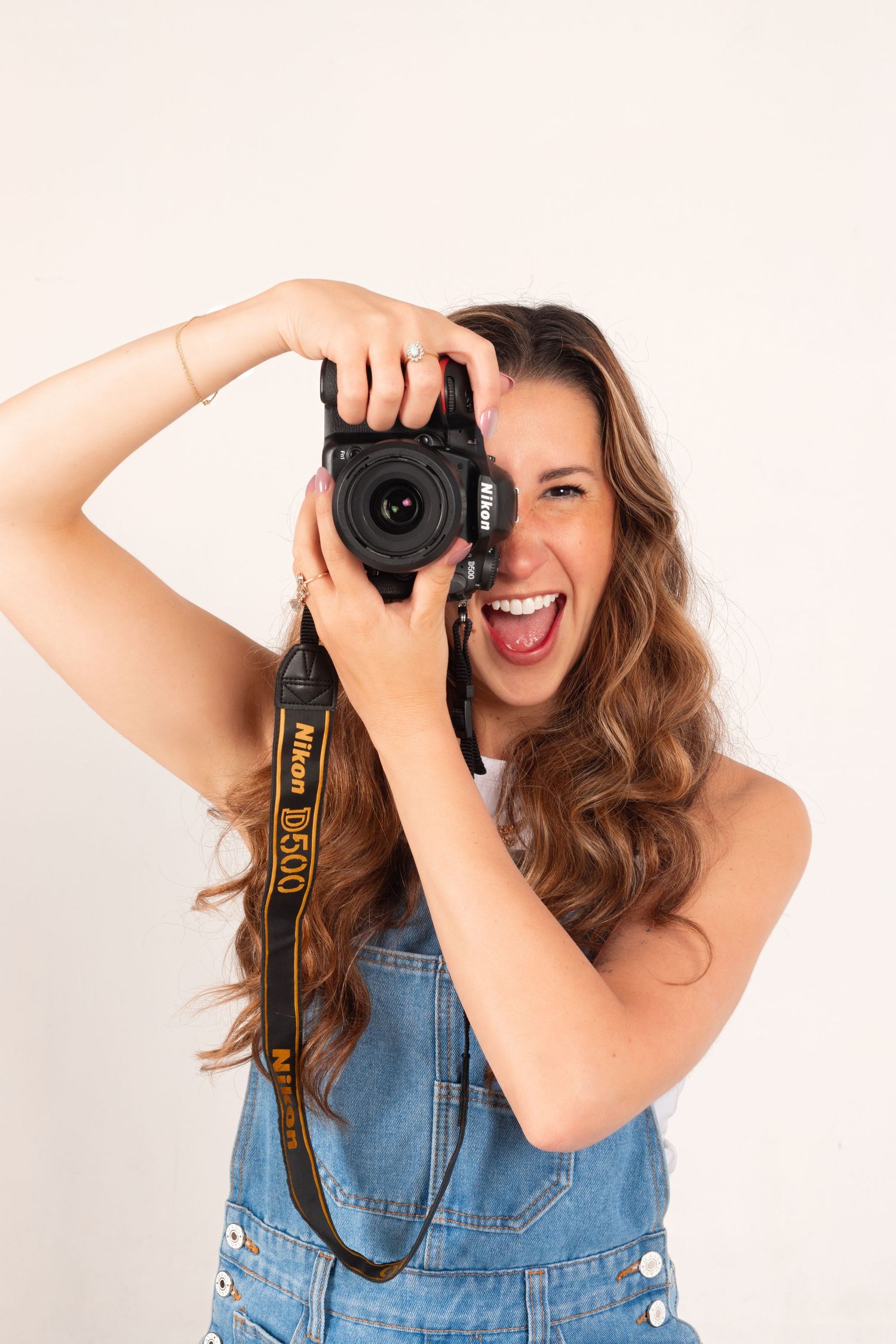 A joyful photographer in denim overalls takes photos with a professional camera.