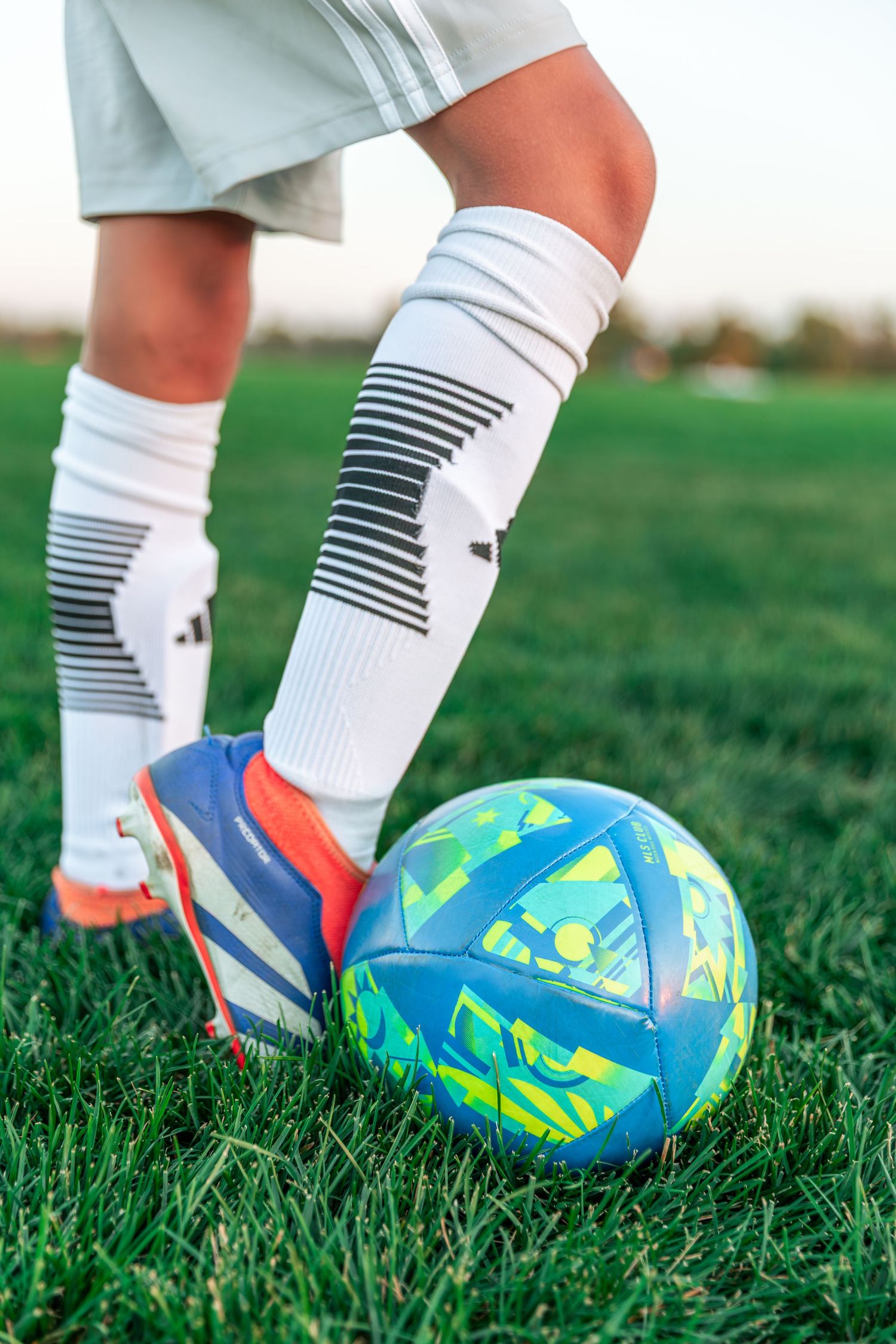 Close-up of soccer player's legs with striped socks and colorful ball on grass field.