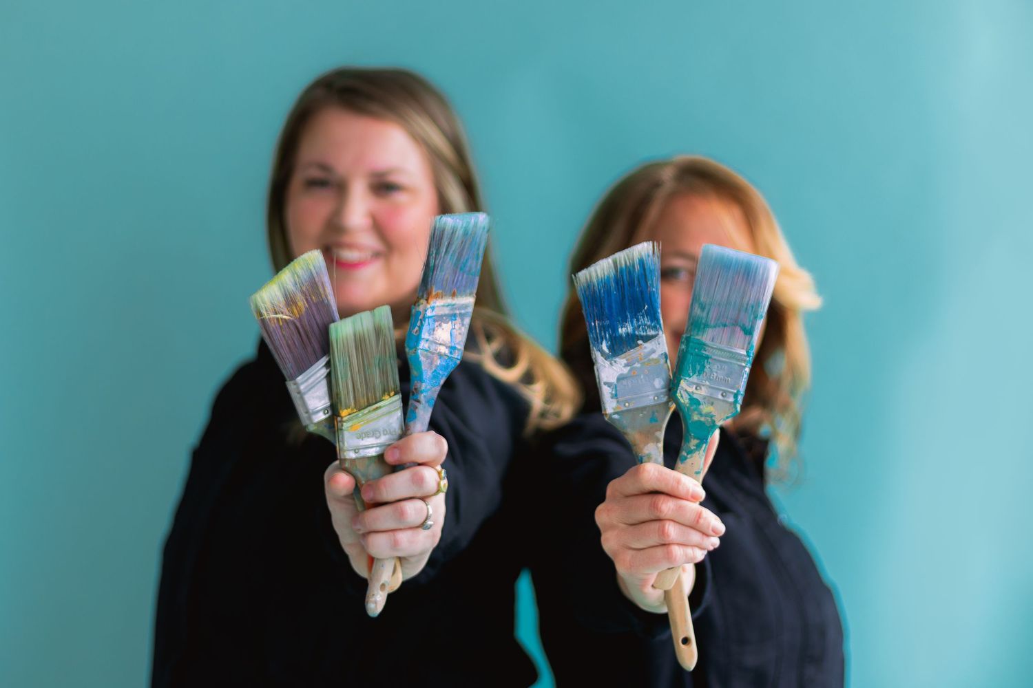Two people holding up colorful cash fans against turquoise background.