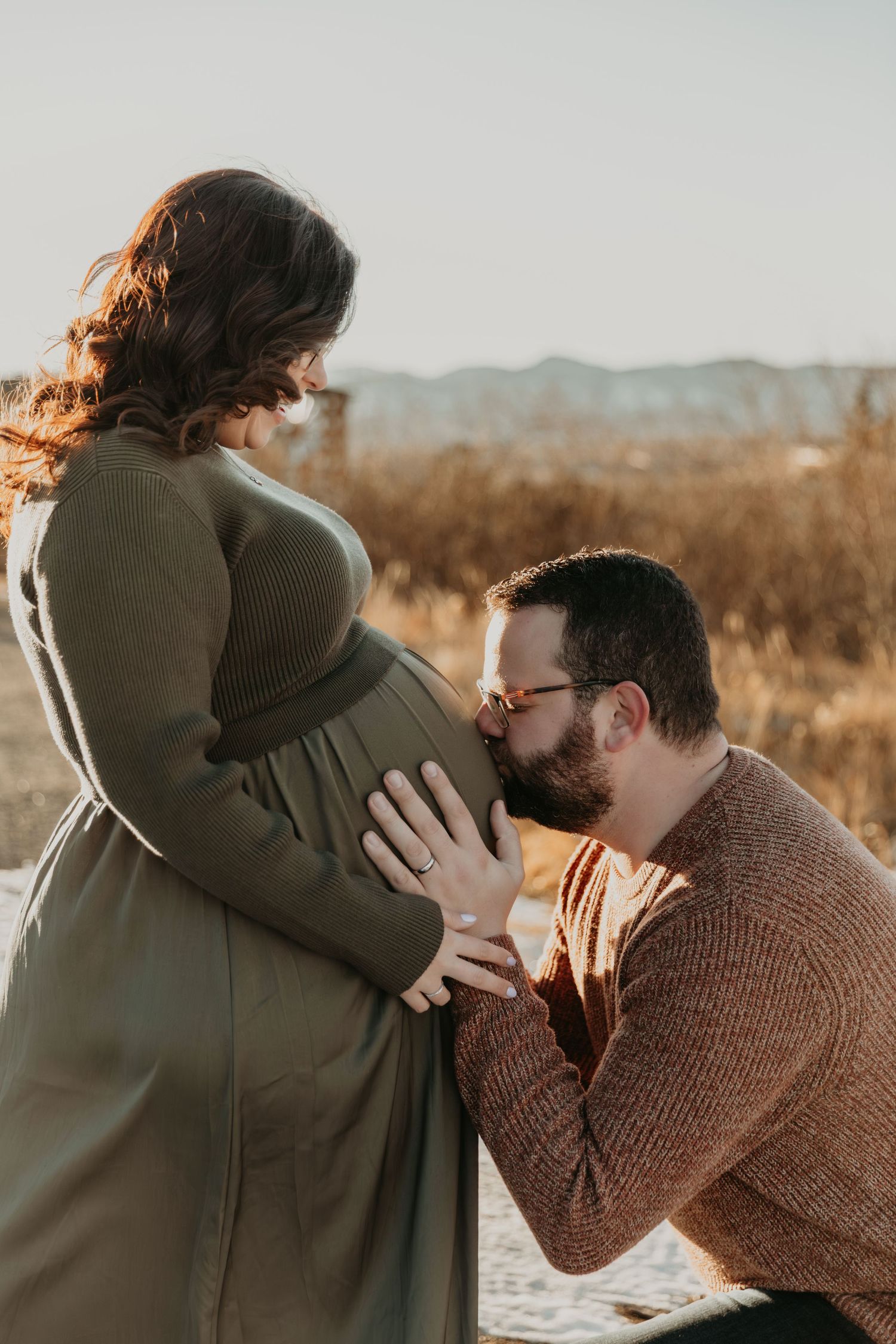 A tender moment between a couple is captured in warm sunset lighting outdoors.