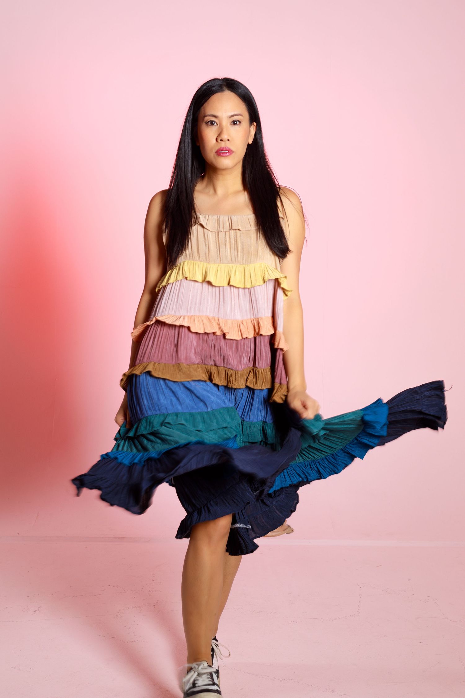 Dynamic twirling pose showcasing flowing movement of multicolored ruffle dress against pink backdrop.