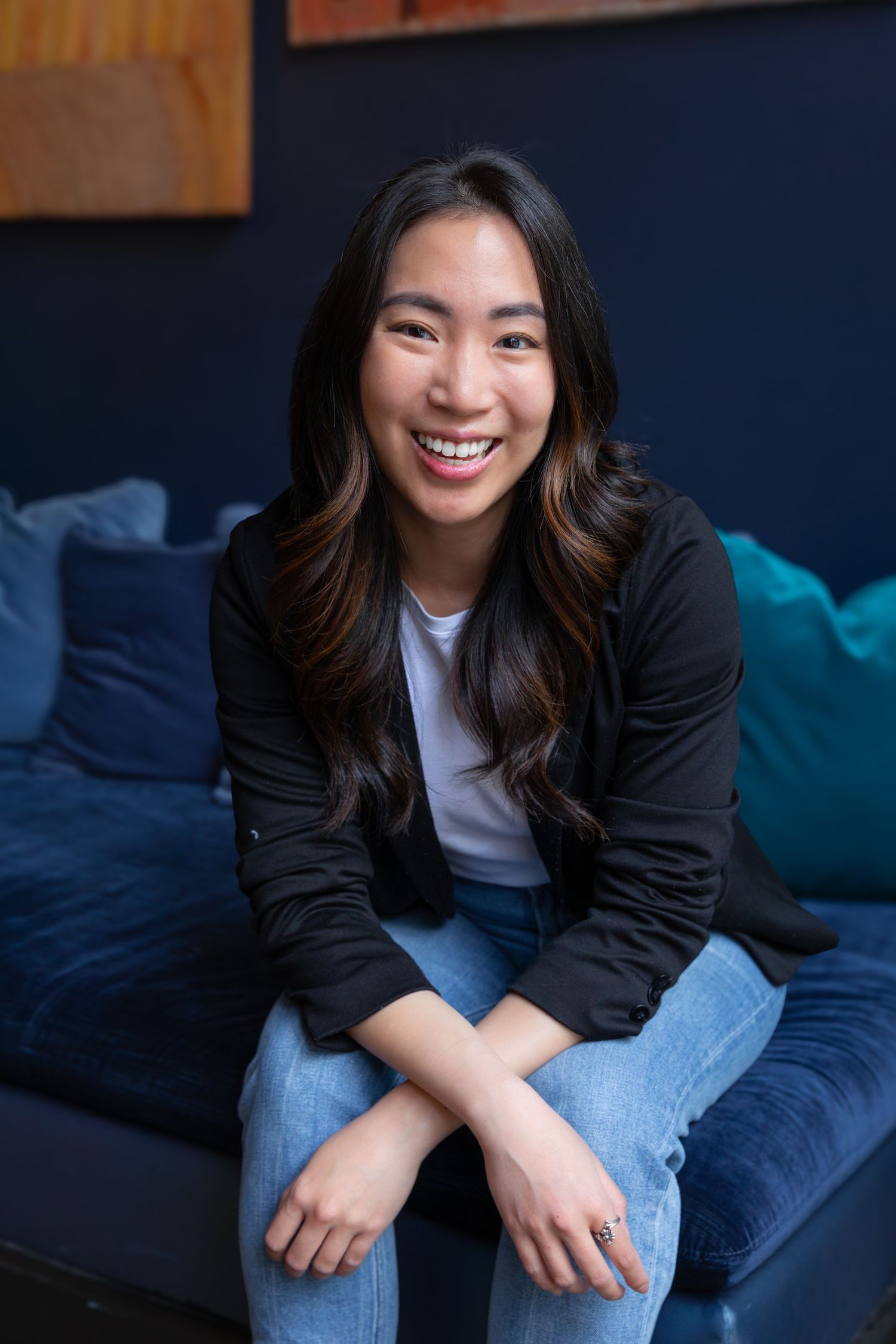 Relaxed lifestyle portraits on blue couch wearing black jacket and jeans.