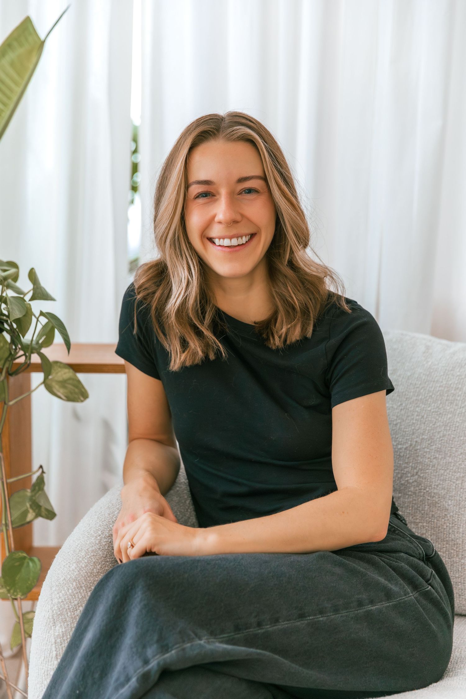 Person in black attire relaxing on a light colored couch with indoor plants in the background.