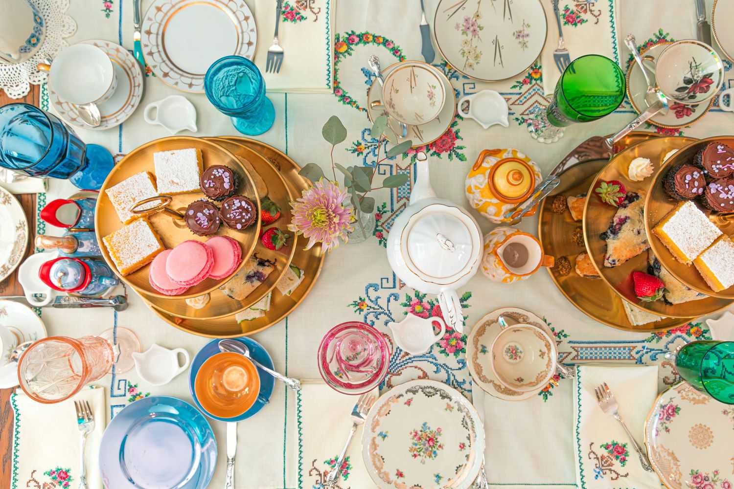Vintage floral plates and colorful glassware arranged on patterned tablecloth.