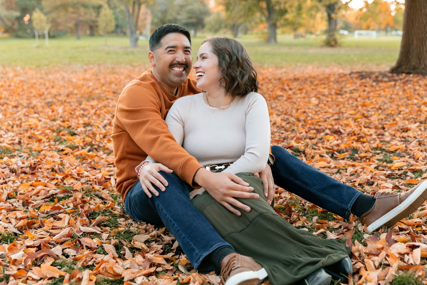 Couple sharing joyful moment together on ground covered in fall foliage.