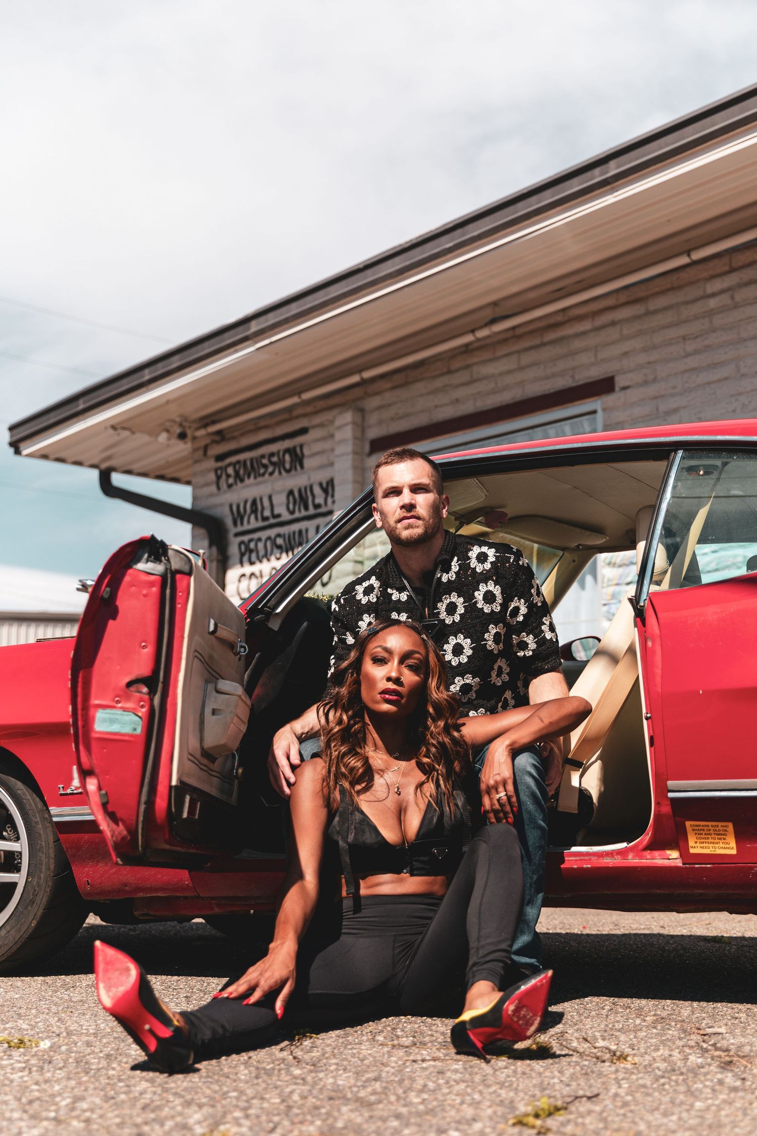 Stylish couple posing with vintage red car in casual urban setting.