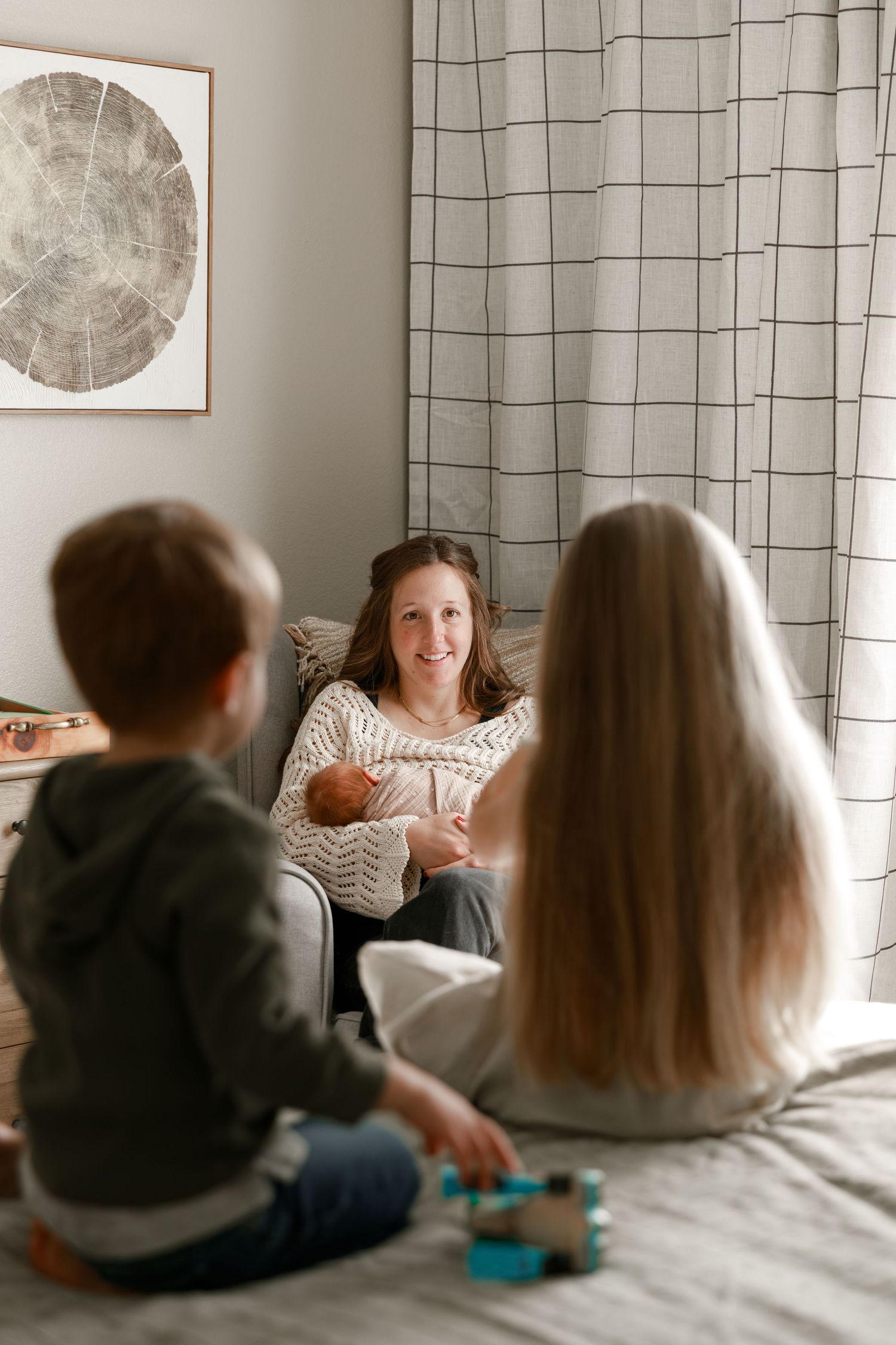Family sitting together on a gray couch in front of striped curtains and wall art.