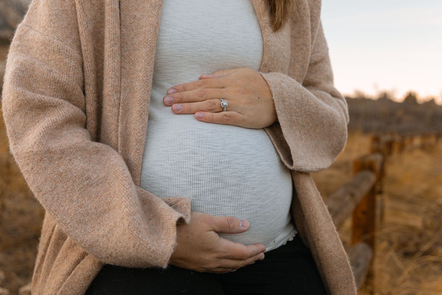 Close-up of hands cradling a pregnant belly while wearing a cozy beige cardigan.