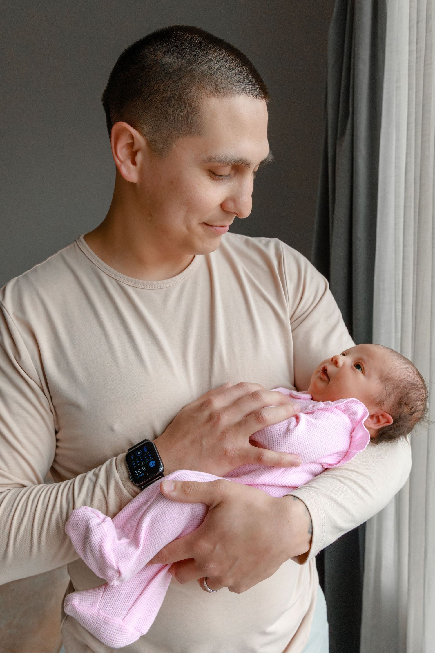 Adult holding newborn baby wearing pink outfit near window.
