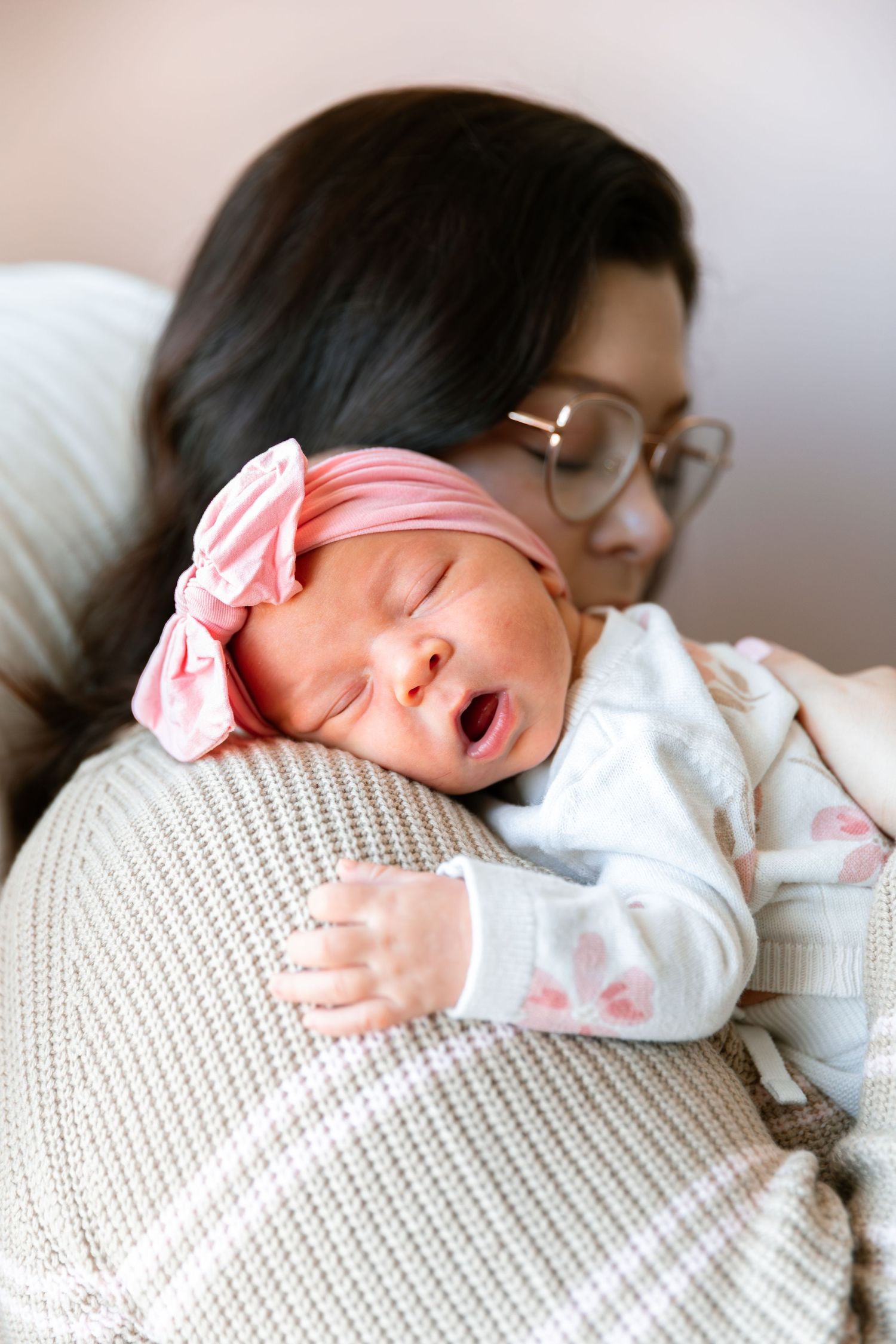 A sleeping newborn baby wearing a pink headband rests peacefully on a white knit blanket.