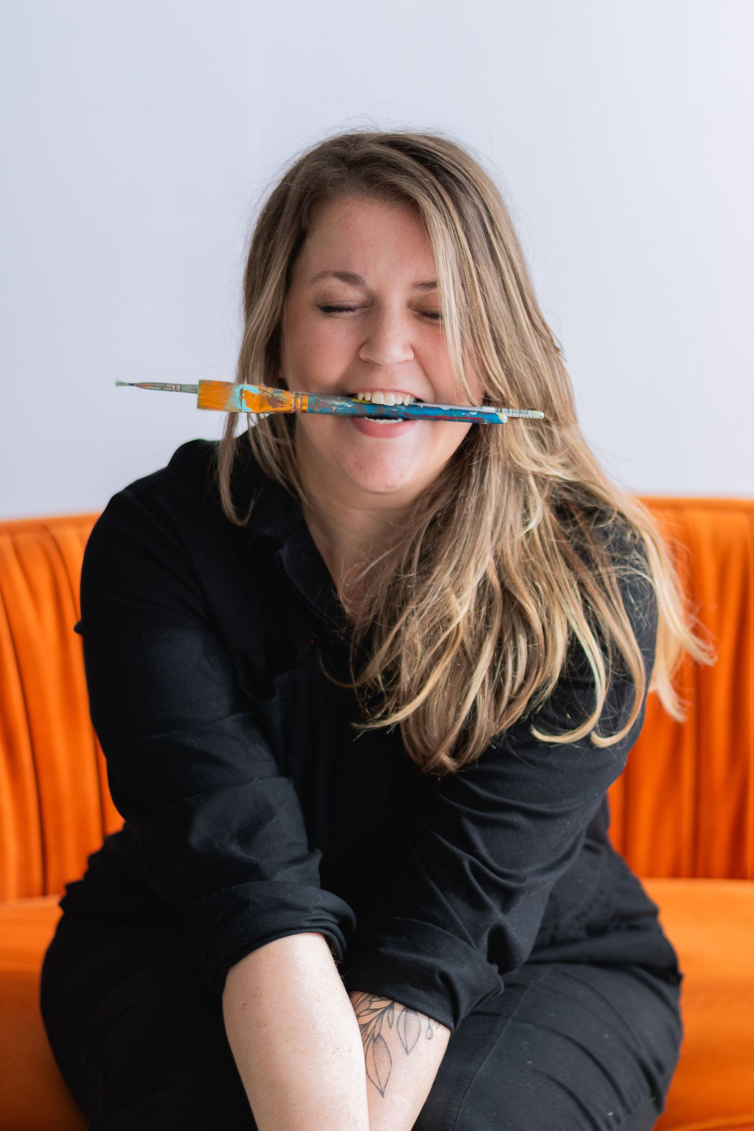 Playful portrait balancing a pencil on nose while sitting on orange couch.