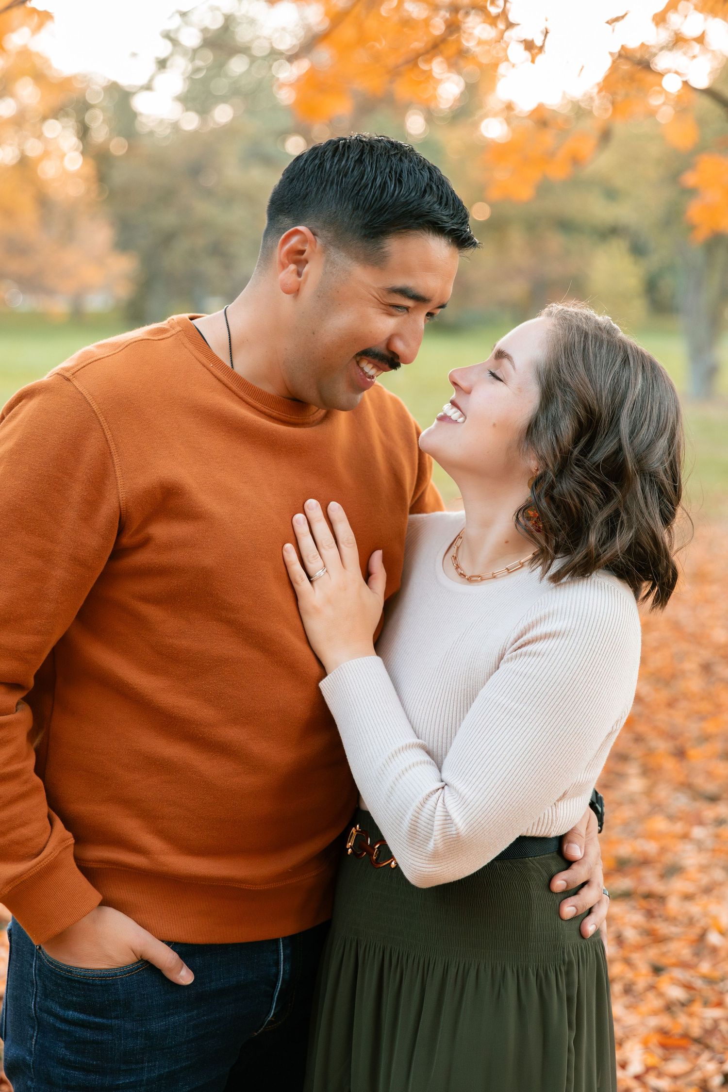 Couple laughing together on autumn ground covered in orange fallen leaves.