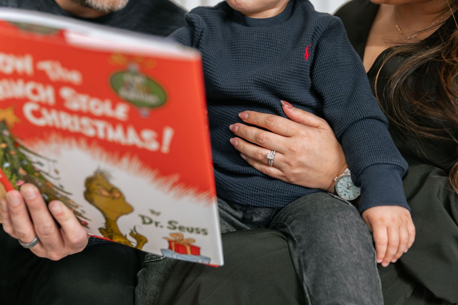 Family reading Dr. Seuss How the Grinch Stole Christmas book with young child during holiday season.