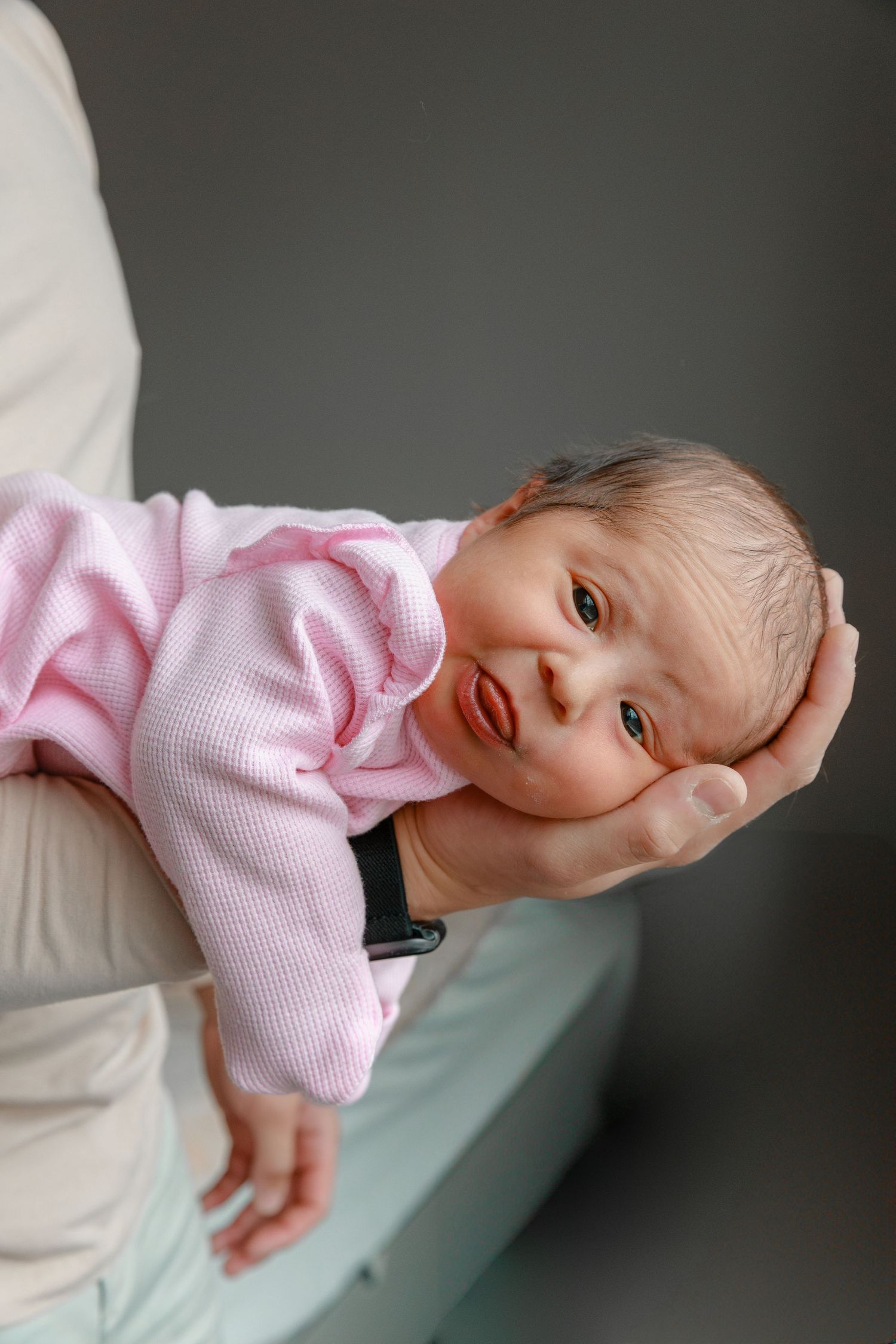 Baby in pink sweater lying on mint green surface.