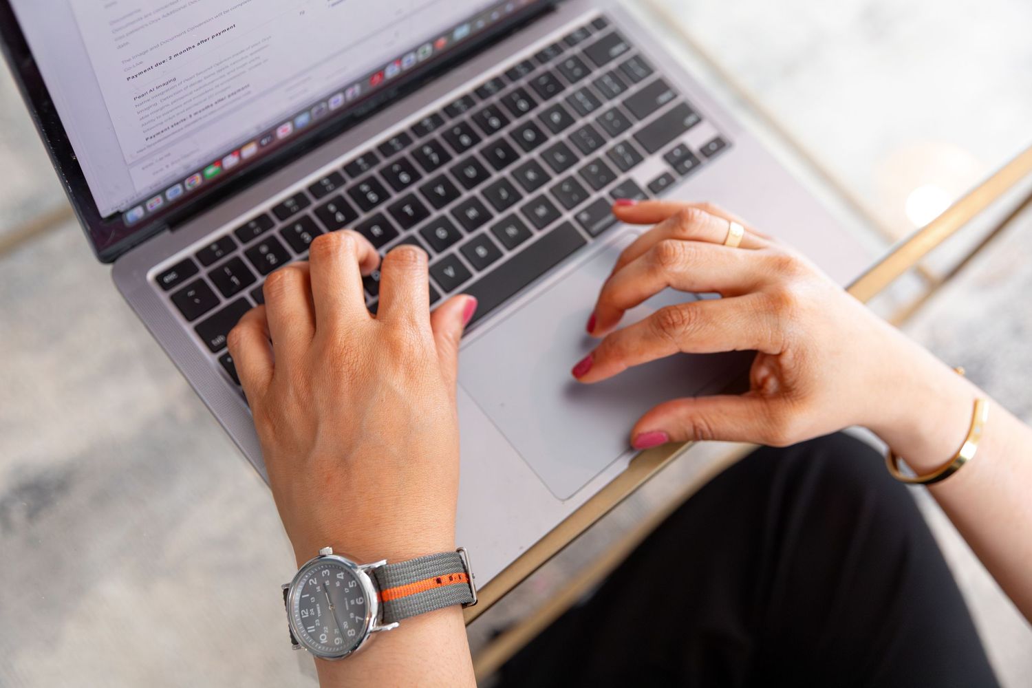 Close-up of hands typing on a laptop keyboard with a watch visible.