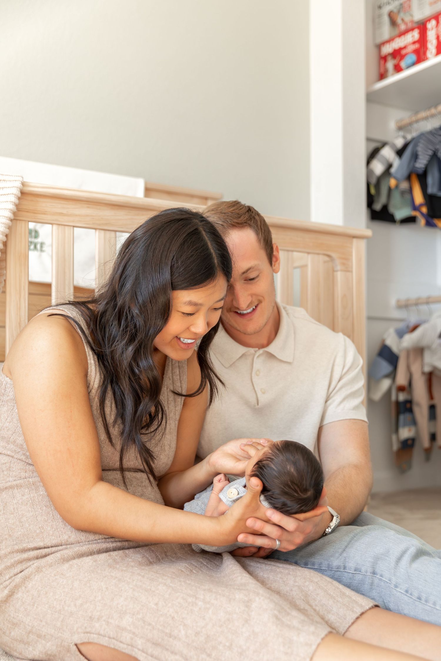 Happy couple smiling at their newborn baby while sitting together on a bedroom floor.
