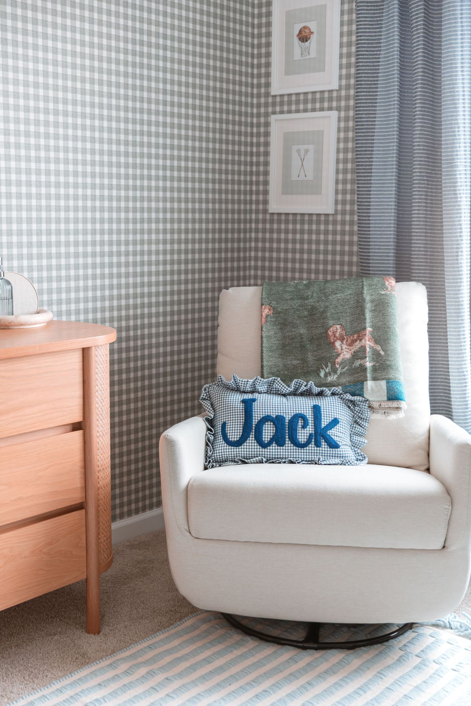 White swivel chair sits in corner of nursery with blue gingham wallpaper and decorative throw pillows.