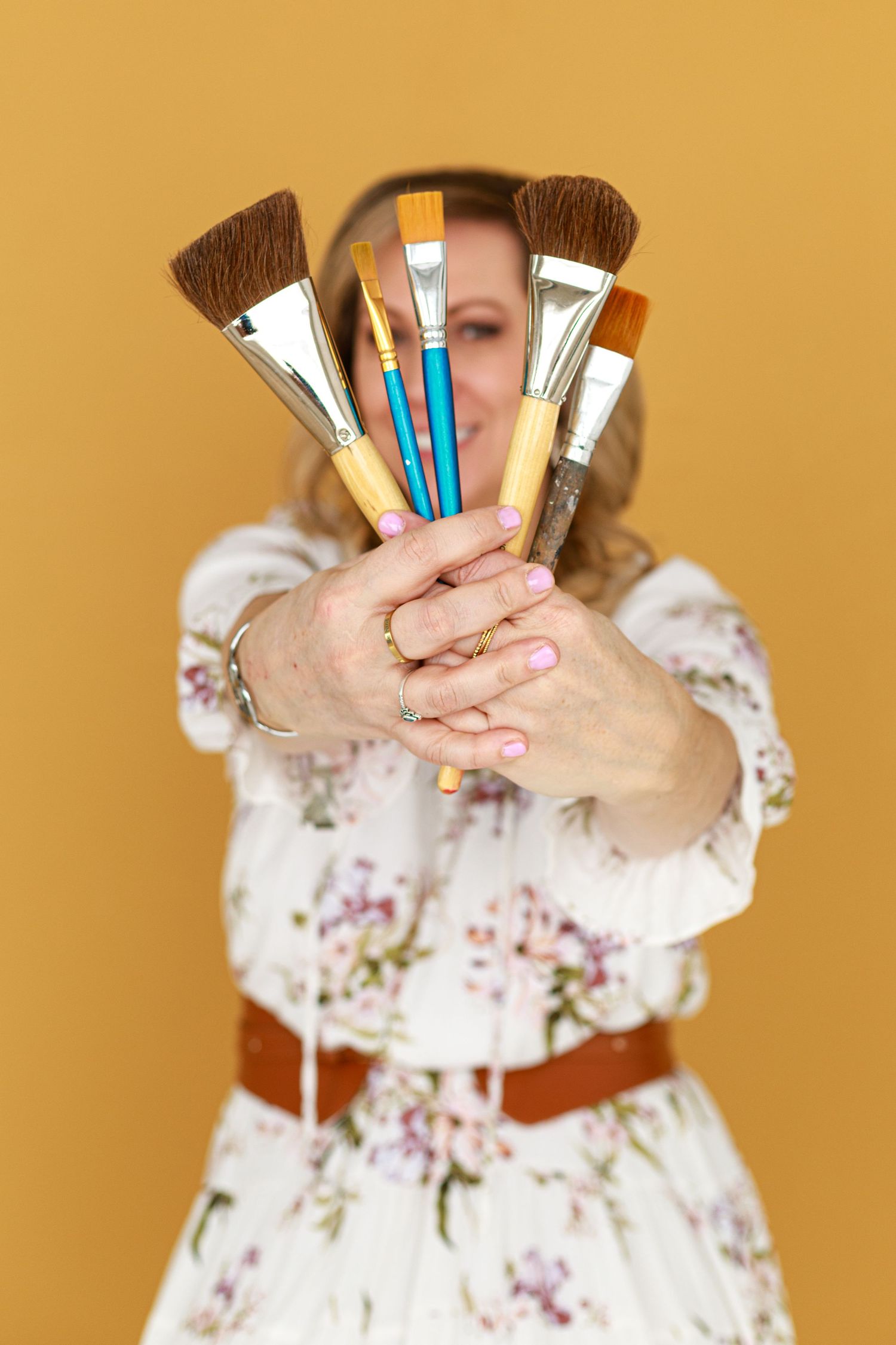 Person holding makeup brushes in fan formation against orange background.