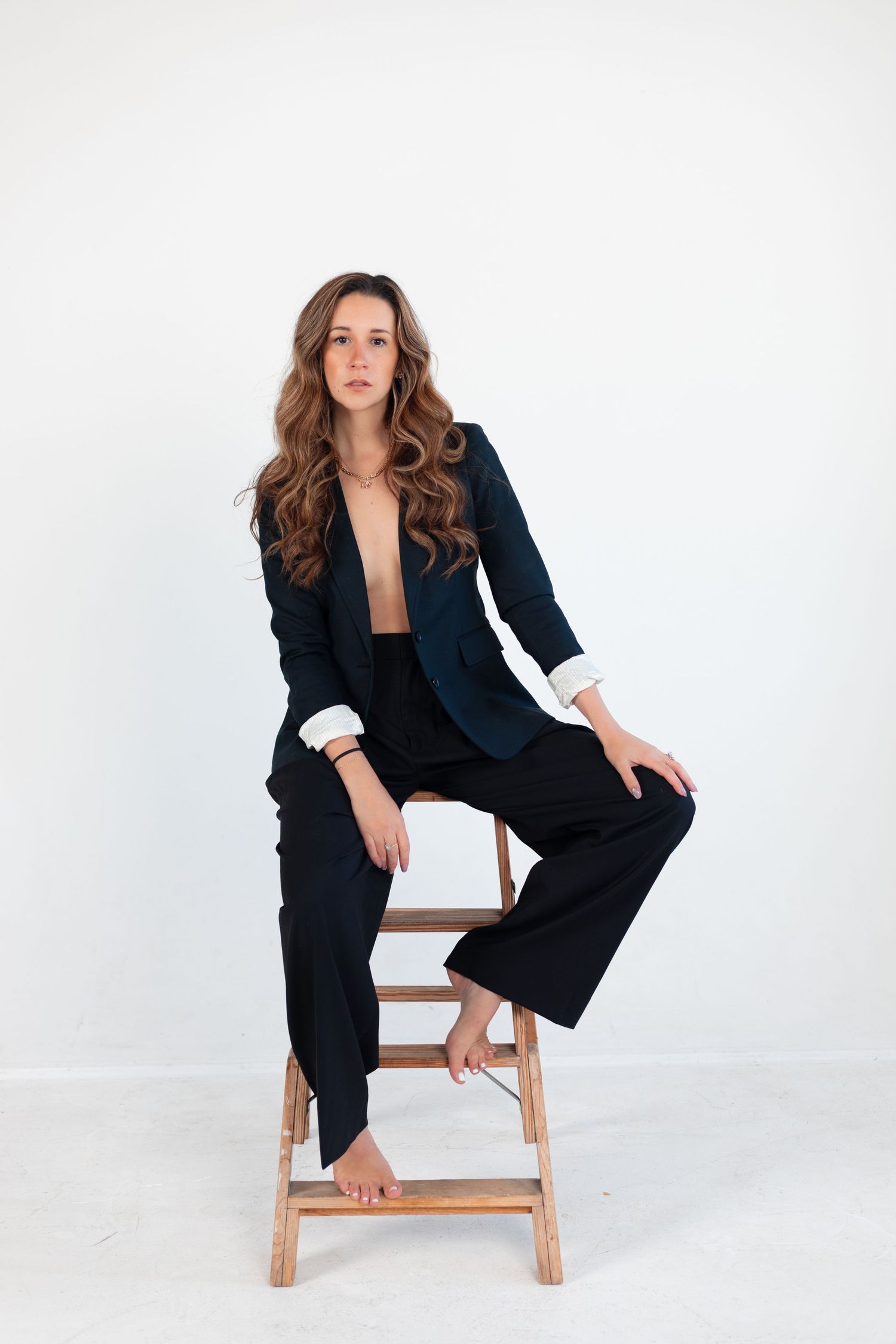 Professional portrait series of a person in a black blazer posing dynamically on a wooden stool.