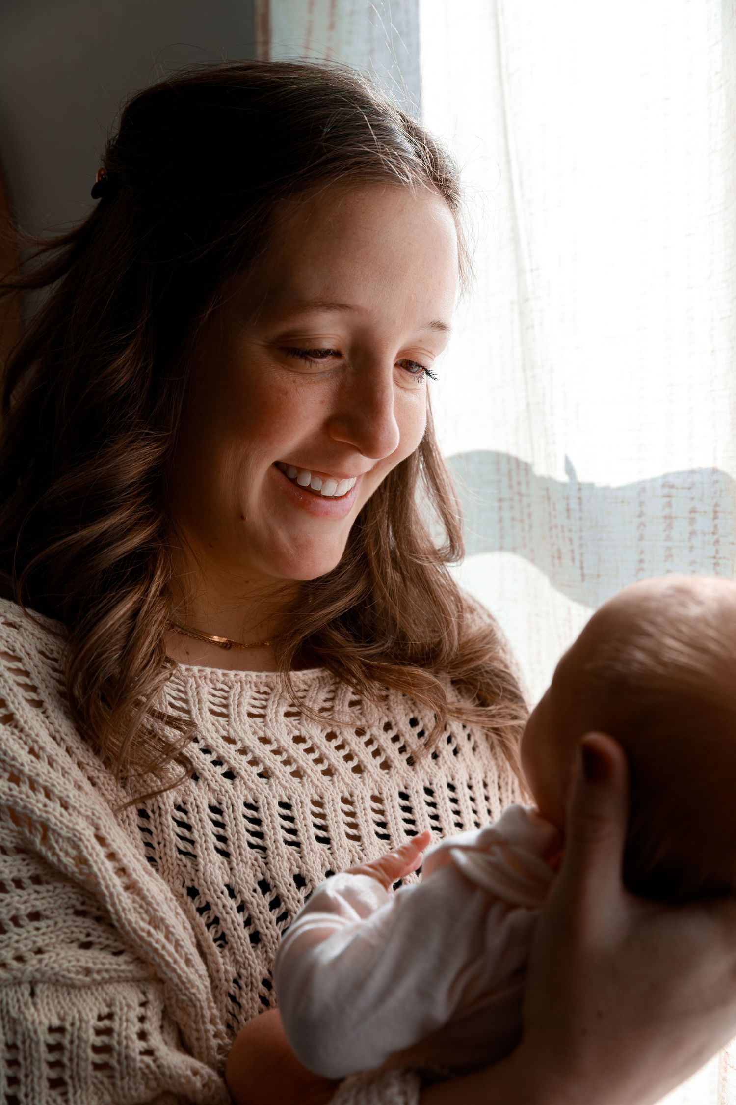 A tender moment captured in soft window light showing a parent holding a newborn baby.