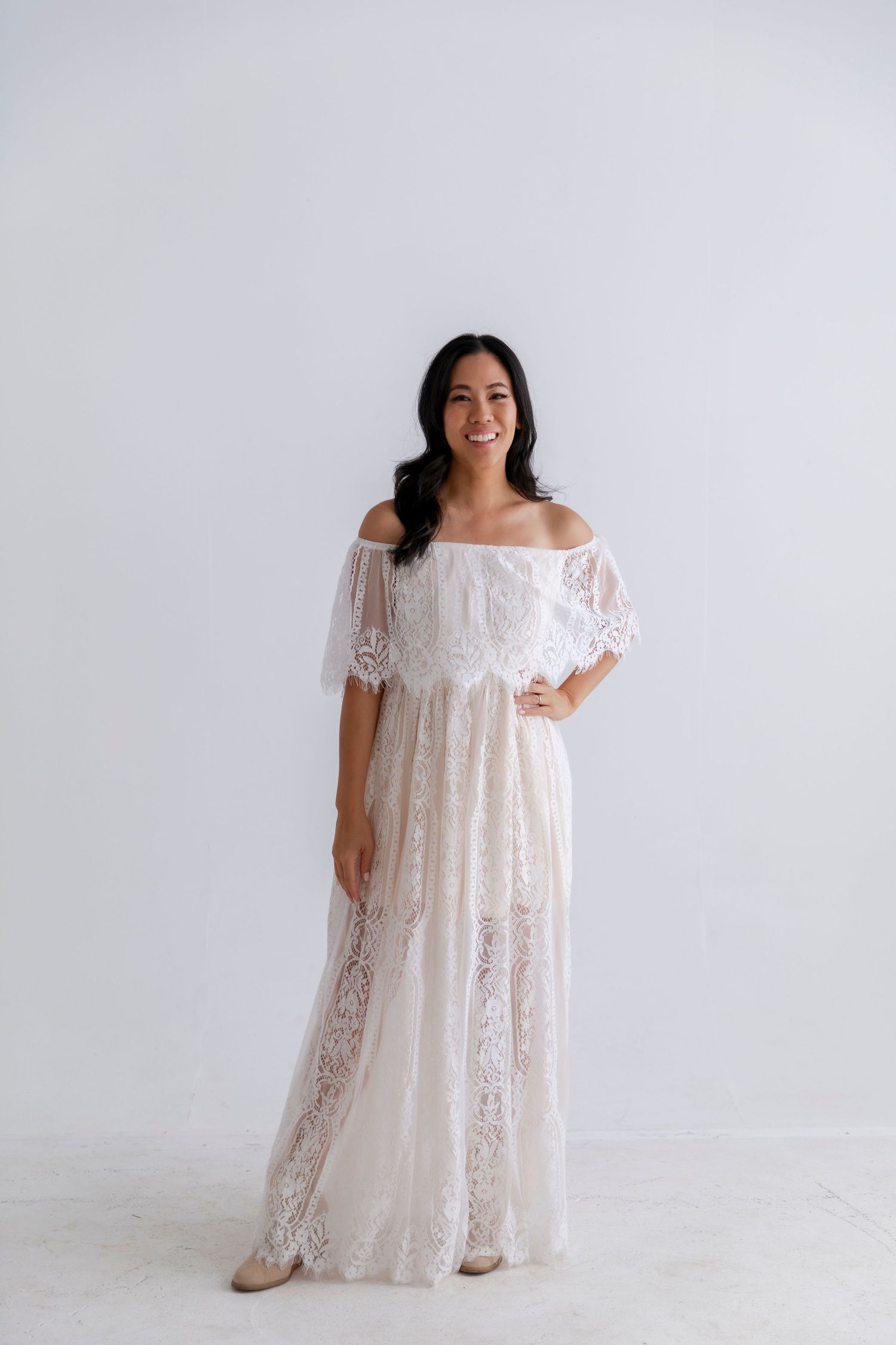 Off-shoulder white lace maxi dress with delicate floral details and sheer overlay.