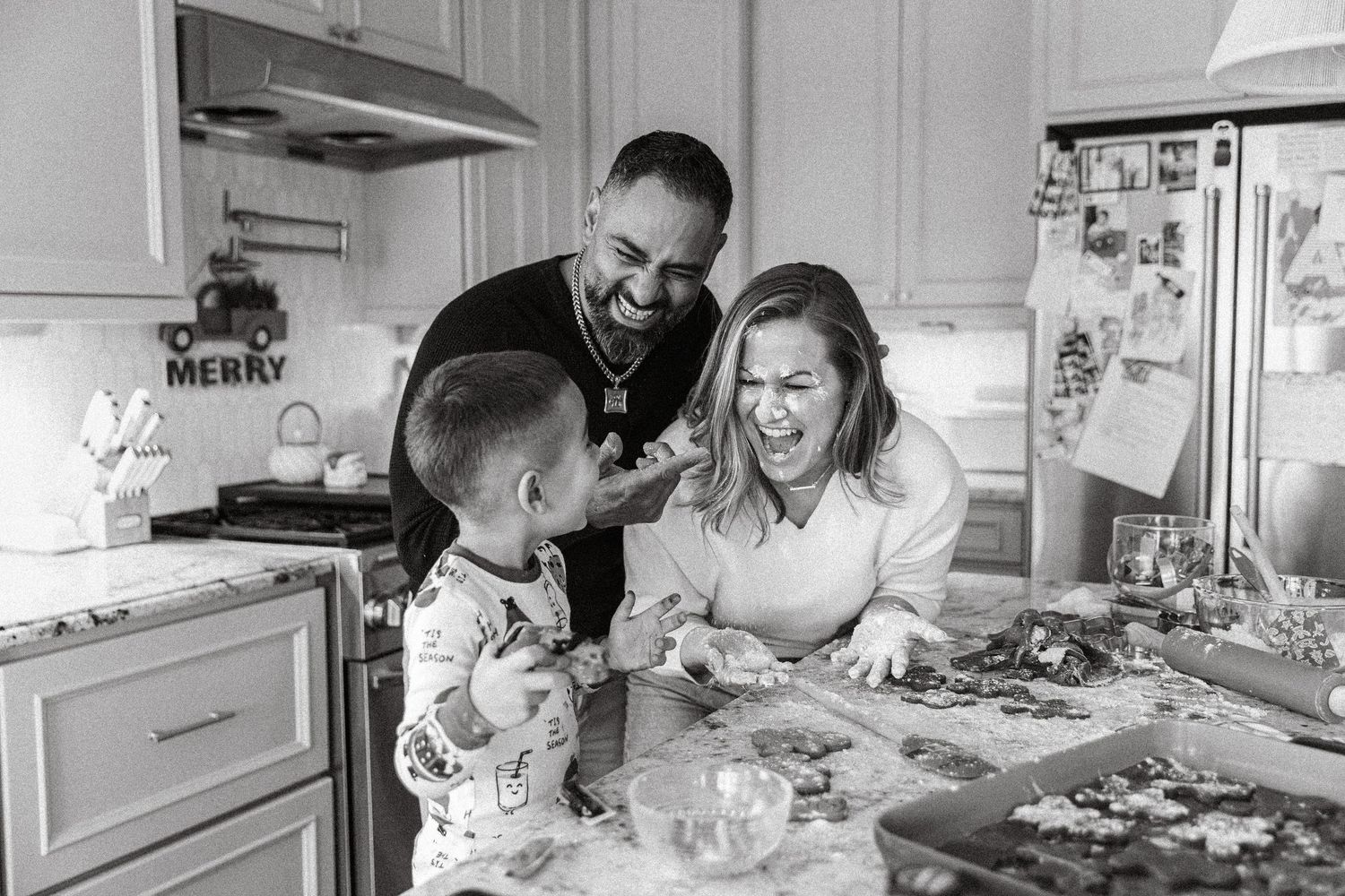 Black and white photo of a joyful family laughing together while doing a puzzle in a cozy kitchen.