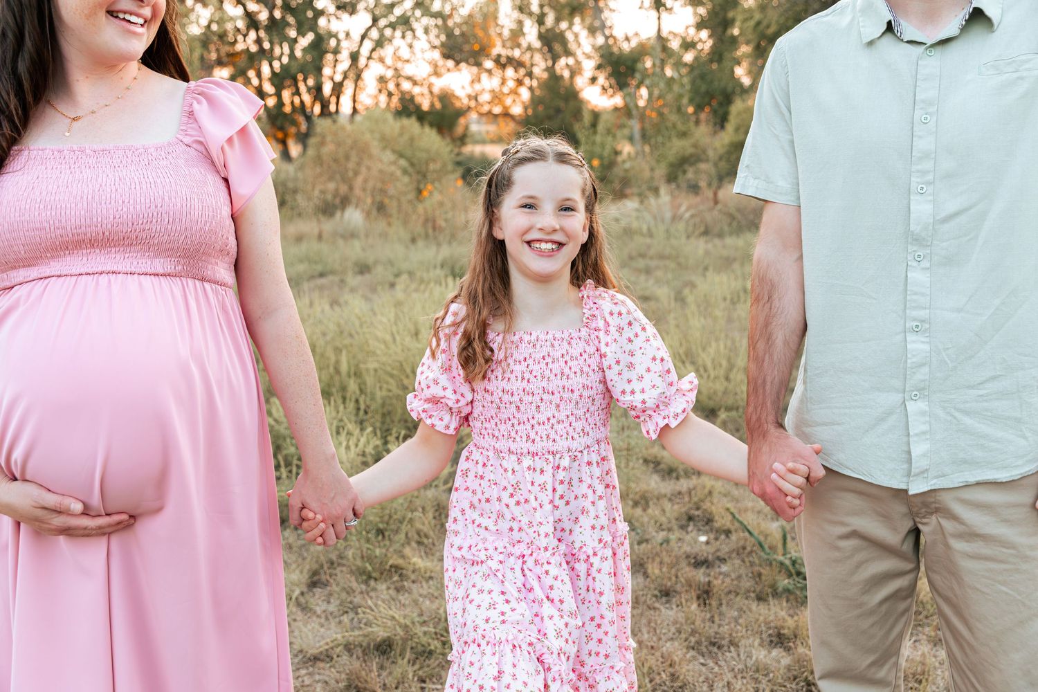 A family in coordinating pink and blue outfits poses together in a grassy field.
