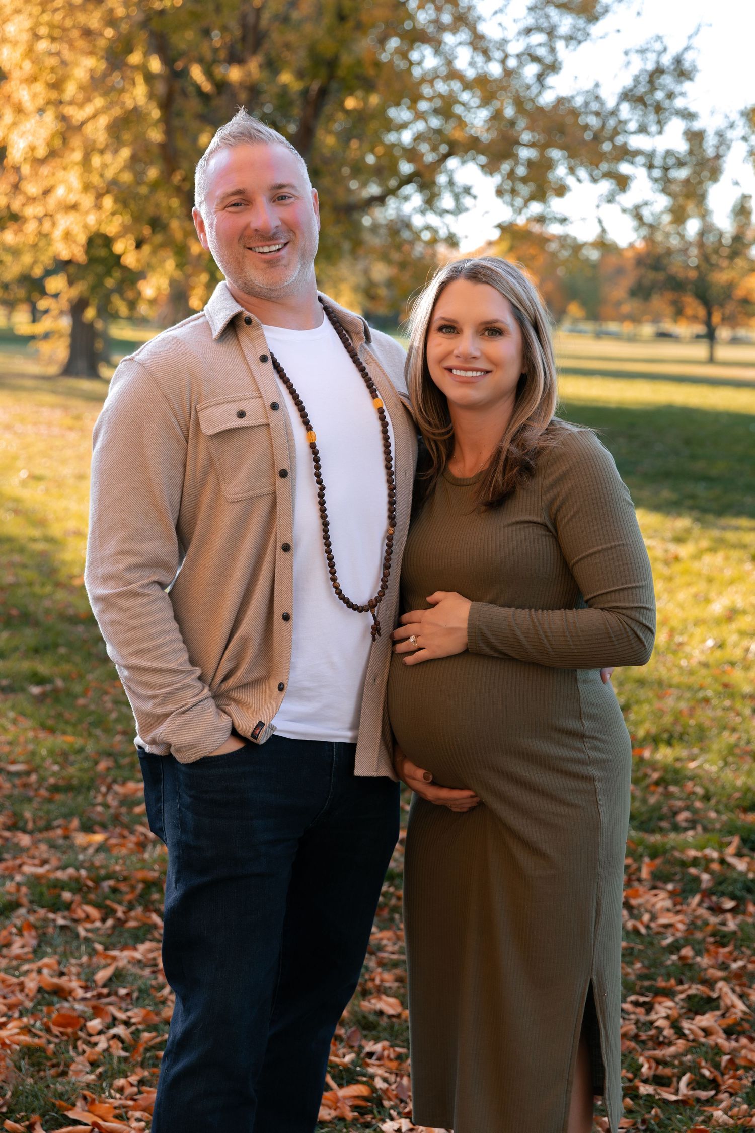 Couple in casual autumn wear posing in park with golden sunlight.