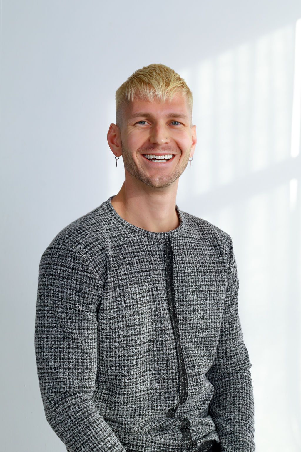 Portrait of someone with blonde hair wearing a grey textured sweater against a white background.